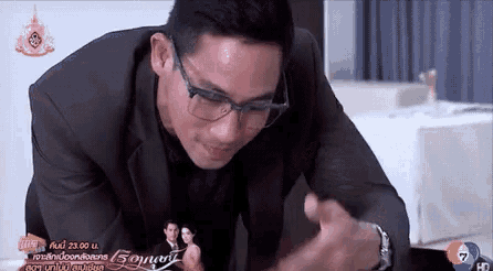 a man wearing glasses sits at a table in front of a sign that says ' sonery ' on it