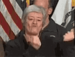 a woman is making a funny face in front of a group of people standing in front of american flags .