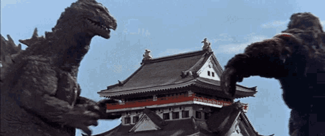 two monsters are standing in front of a building and one of them has the word king kong on its head