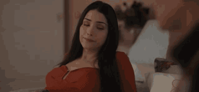 a woman is sitting on a bed with her eyes closed and a red top on .