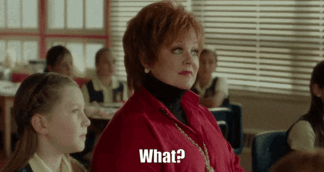 a woman in a red shirt is sitting in a classroom next to a little girl and says " what "