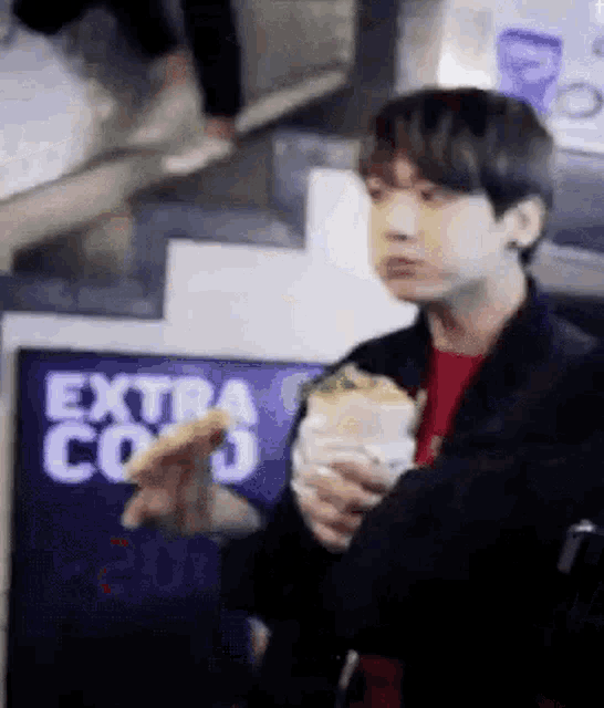 a young man is eating a sandwich in front of a sign that says extra coo .