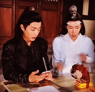 two men are sitting at a table one is looking at his phone
