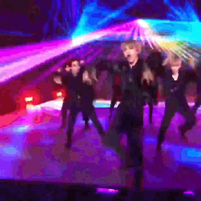 a group of people dancing on a stage with purple and blue lights