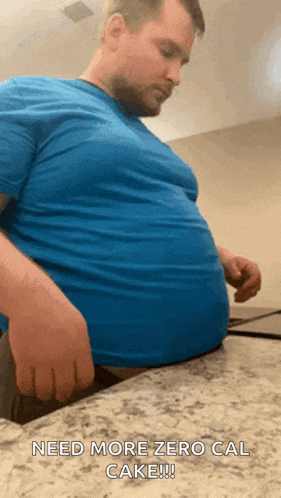a man in a blue shirt is sitting on a counter and says " need more zero cal cake !!! "