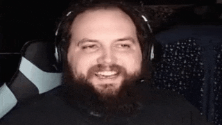 a man with a beard wearing headphones is smiling while sitting in a chair .