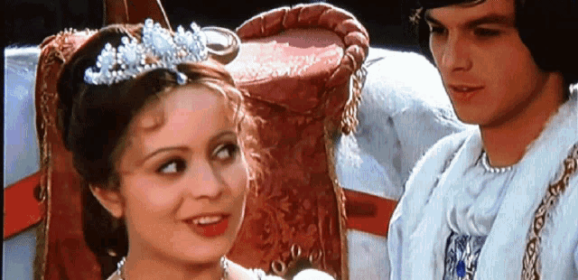 a woman wearing a tiara sits next to a man in a white coat