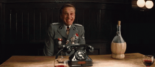 a man in a military uniform is sitting at a table with a telephone and a glass of wine .