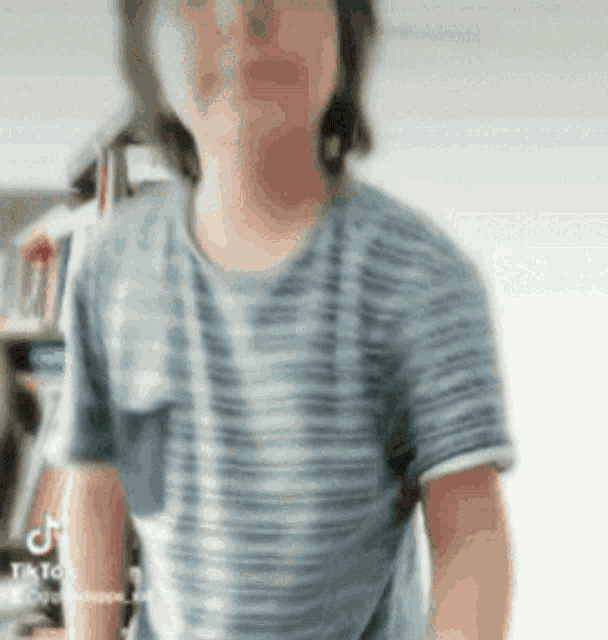 a person wearing a striped shirt is standing in front of a bookshelf .