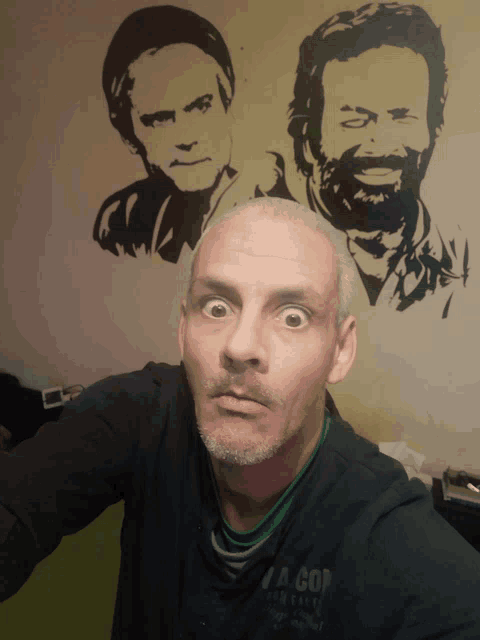 a man taking a selfie in front of a wall with portraits of two men on it