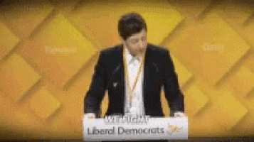 a man in a suit stands at a podium with a sign that says liberal democrats