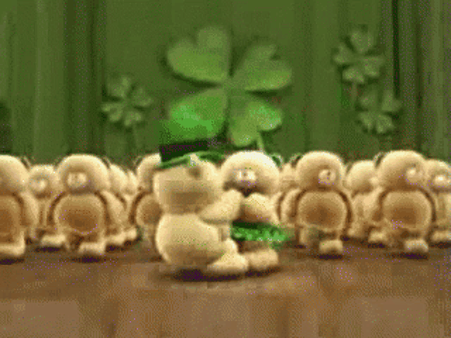 a group of stuffed animals are dancing in front of a clover on a wall