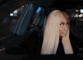 a woman with long blonde hair is sitting in a car looking out the window .