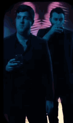 two men are standing in a dark room and one is covering his mouth with his hand