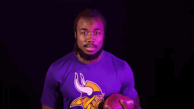 a man in a purple shirt with a vikings logo holds a football