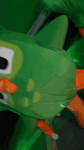 a green stuffed animal with orange feet and a white face