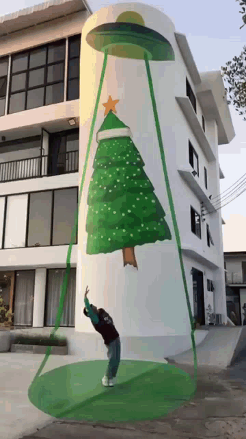 a man stands in front of a large christmas tree painting