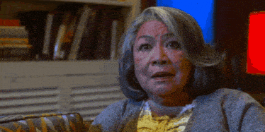 a woman with gray hair is sitting on a couch with a bookshelf in the background