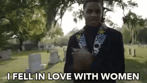 a man is standing in a cemetery with the words `` i fell in love with women '' written on the ground .