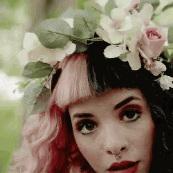 a woman with pink hair and a flower crown on her head is looking at the camera .