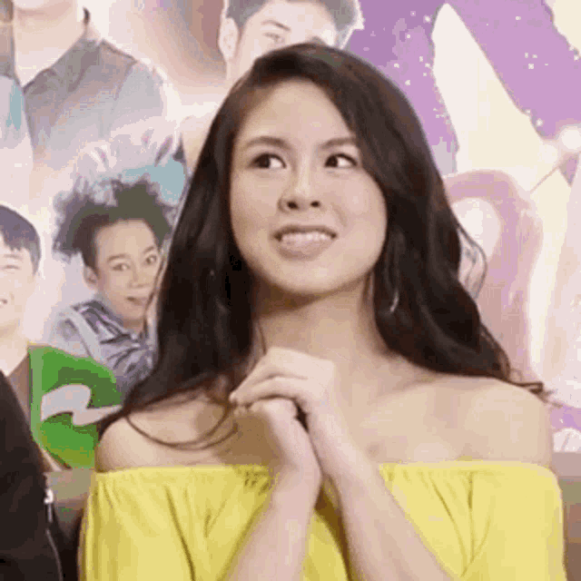 a woman in a yellow off the shoulder top is smiling and looking at the camera .
