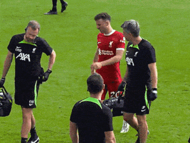 a man in a red shirt that says ' standard chartered ' on it shakes hands with two other men