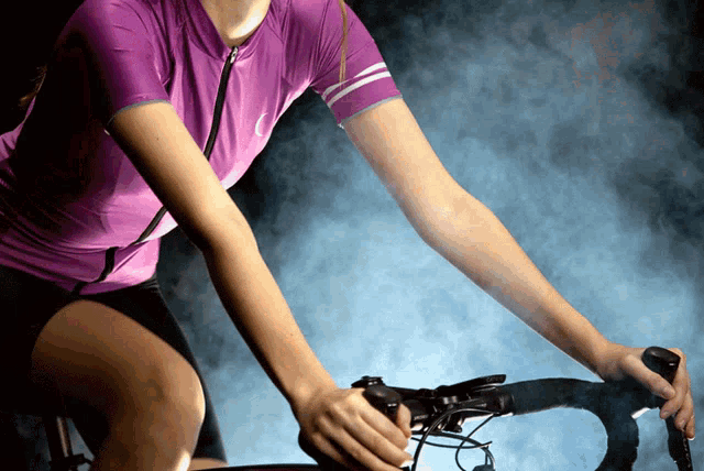 a woman in a purple shirt is riding a bike in the dark
