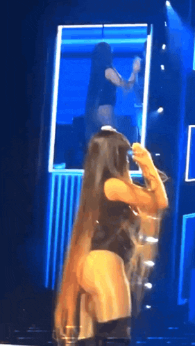 a woman with long hair is standing in front of a mirror on stage