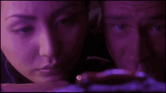 a man and a woman are looking at something in a dark room in a purple light .
