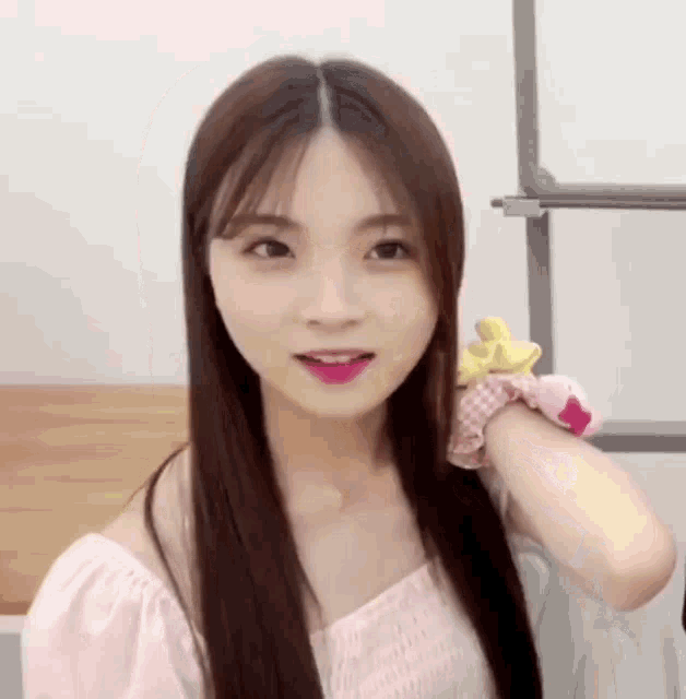 a young woman with long hair is wearing a pink top and a yellow scrunchie .