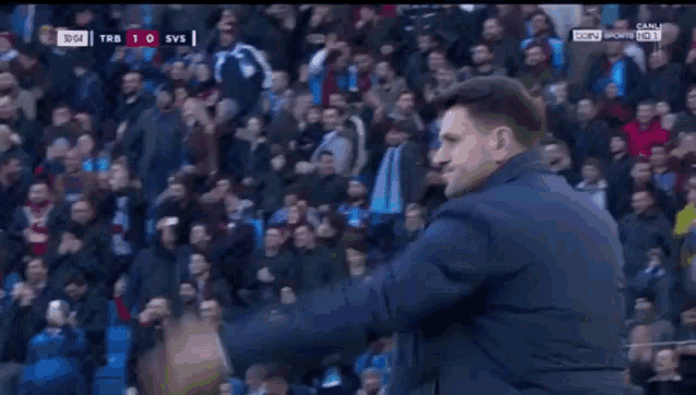 a man in a blue jacket stands in front of a crowd at a soccer match