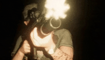 a man is holding a shotgun in his hand in the dark and shooting it .