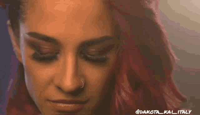 a woman with pink hair and a nose ring looks at the camera