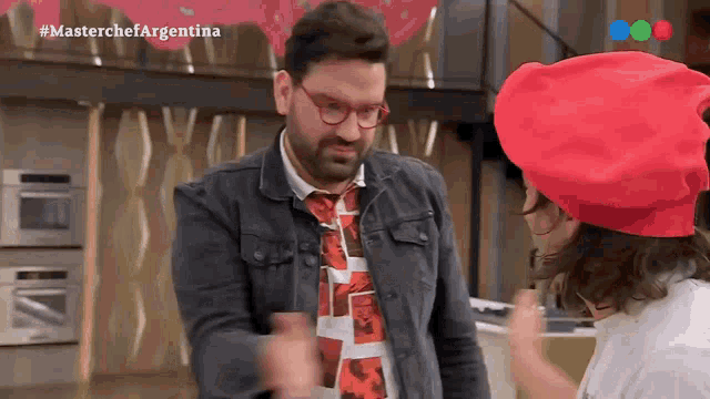 a man wearing glasses and a red hat is talking to a woman wearing a red hat