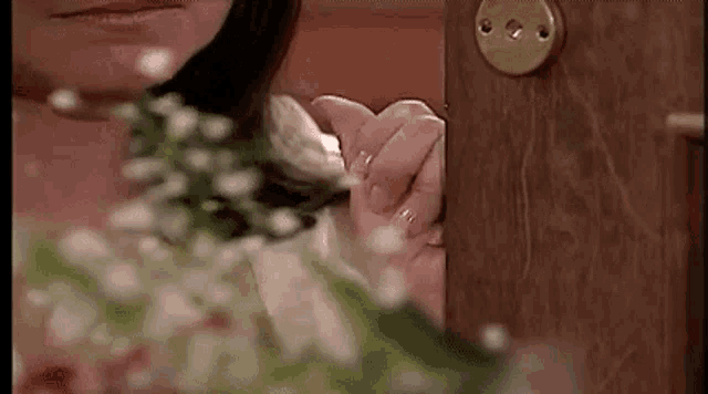 a woman is holding a bouquet of flowers in her hand while standing next to a wooden door .