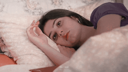 a woman in a purple shirt is laying on a bed looking at the camera