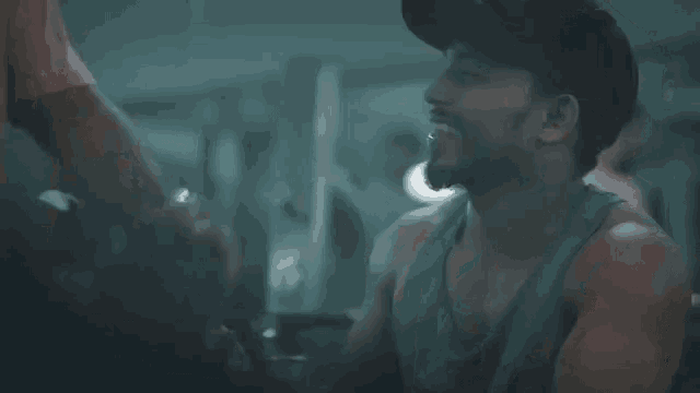 a man wearing a baseball cap is sitting in a gym talking to another man .