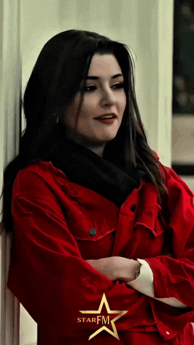 a woman in a red jacket is leaning against a wall with her arms crossed and the word starfm on the bottom