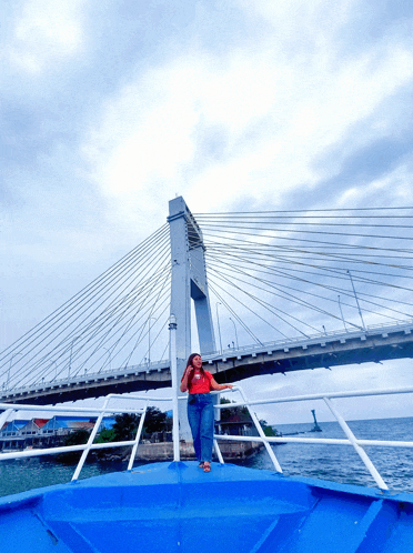 a woman stands on a boat in front of a large bridge