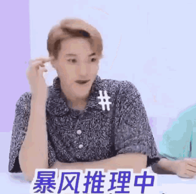 a man with chinese writing on his shirt is sitting at a table with his arms crossed and making a funny face .