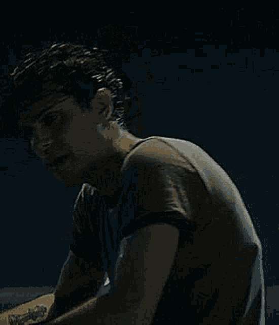 a man with curly hair is sitting down in a dark room looking at the camera .