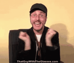 a man wearing glasses and a hat is sitting in a chair with his hands in the air .