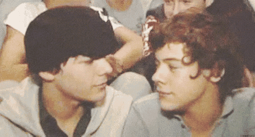 two young men are sitting next to each other and looking at each other . one of the men is wearing a hat .