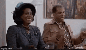 a man and a woman are sitting at a table . the woman is wearing a hat .