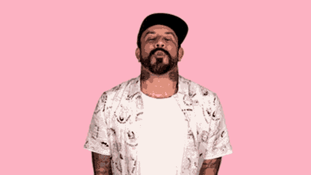 a man with a beard and tattoos is wearing a white shirt and a black hat