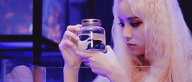 a blonde woman is holding a jar of water with a fish in it .