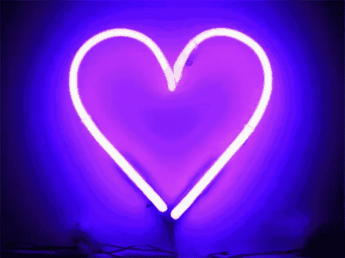 a purple neon heart is lit up on a dark background