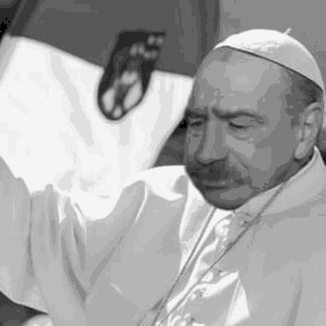 a black and white photo of a man with a mustache wearing a white robe and a white hat .