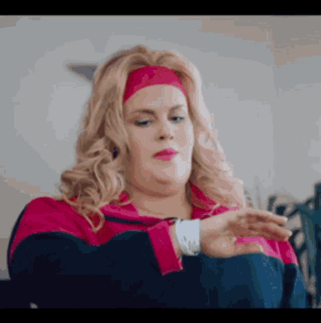 a woman wearing a headband and a pink sweatshirt is stretching her arms .