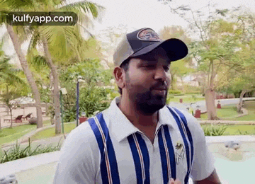 a man wearing a baseball cap and a striped shirt is standing in a park .